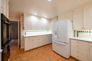 Kitchen featuring white cabinets, white fridge with ice dispenser, tasteful backsplash, and light parquet floors