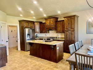 Kitchen with decorative backsplash, light stone countertops, a kitchen island with sink, light tile patterned floors, and stainless steel appliances