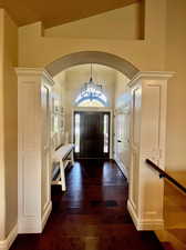 Foyer featuring vaulted ceiling, ornate columns, an inviting chandelier, and dark hardwood / wood-style floors