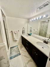 Bathroom with a textured ceiling, an enclosed shower, dual bowl vanity, and tile patterned floors