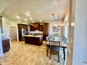 Kitchen featuring an island with sink, light stone countertops, a notable chandelier, light tile patterned flooring, and hanging light fixtures