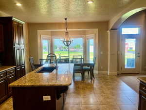 Kitchen featuring a wealth of natural light, light tile patterned flooring, an island with sink, and a chandelier