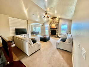 Carpeted living room featuring ceiling fan, a stone fireplace, a textured ceiling, and lofted ceiling