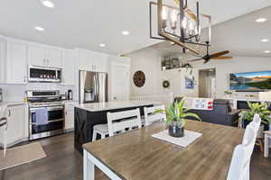 Dining space featuring dark wood-type flooring, ceiling fan with notable chandelier, and vaulted ceiling