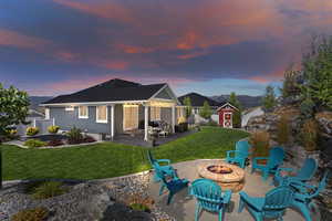 Back house at dusk with a lawn, an outdoor fire pit, a storage shed, and a patio