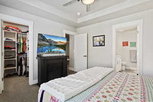 Carpeted bedroom with a tray ceiling, ensuite bath, a spacious closet, a closet, and ceiling fan