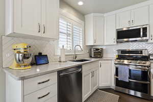 Kitchen featuring backsplash, white cabinets, light stone countertops, sink, and stainless steel appliances