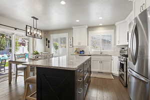 Kitchen with a center island, appliances with stainless steel finishes, dark wood-type flooring, decorative backsplash, and white cabinetry