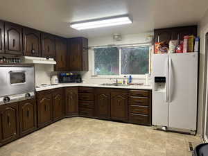 Kitchen featuring sink, light tile patterned flooring, white appliances, and dark brown cabinets