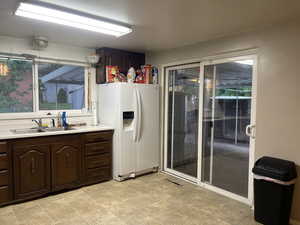 Kitchen with light tile patterned flooring, sink, dark brown cabinetry, and white refrigerator with ice dispenser