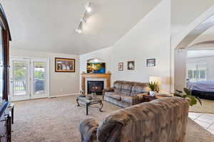 Living room featuring light colored carpet, high vaulted ceiling, track lighting, a tiled fireplace, and a textured ceiling