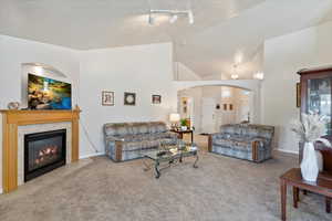 Carpeted living room featuring rail lighting, a textured ceiling, a tiled fireplace, and lofted ceiling