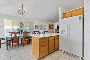 Kitchen featuring decorative light fixtures, white refrigerator with ice dispenser, a chandelier, light tile patterned floors, and kitchen peninsula