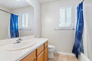 Full bathroom with tile patterned flooring, shower / bath combination with curtain, vanity, and toilet