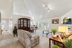 Carpeted living room with french doors, a textured ceiling, track lighting, and lofted ceiling