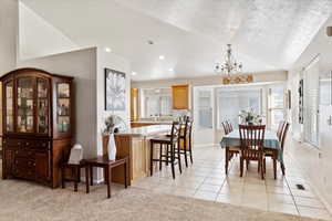 Carpeted dining room featuring a notable chandelier, vaulted ceiling, and a textured ceiling