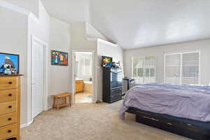 Bedroom featuring lofted ceiling, light colored carpet, and ensuite bath