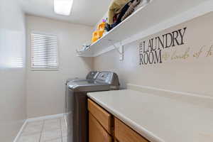 Clothes washing area with light tile patterned flooring and washing machine and dryer