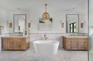 Bathroom featuring a bath,  carrara marble tile patterned floors, vaulted ceiling, double vanity, and tile walls