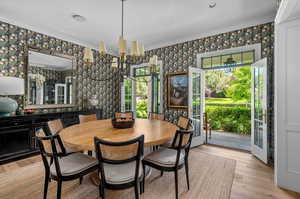 Dining area with a notable chandelier, light hardwood / wood-style floors, crown molding, and french doors