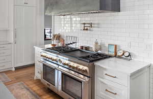 Kitchen with double oven range, light hardwood / wood-style floors, light stone countertops, and backsplash.  6 burners and griddle