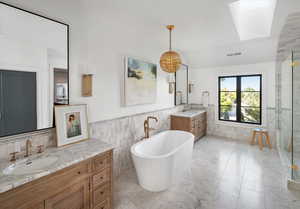 Bathroom featuring  carrara marble tile patterned flooring, tile walls, a tub to relax in, and vanity