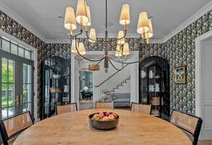 Dining space with plenty of natural light, ornamental molding, an inviting chandelier, and french doors