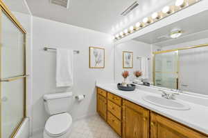 Full bathroom featuring tile patterned flooring, toilet, vanity, and enclosed tub / shower combo