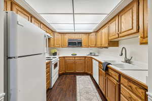 Kitchen with sink, dark wood-type flooring,  and white appliances