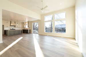 Unfurnished living room with a towering ceiling, ceiling fan, and light wood-type flooring