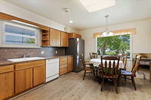 Kitchen featuring stainless steel refrigerator, sink, tasteful backsplash, light wood-type flooring, and white dishwasher