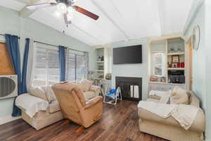 Living room featuring ceiling fan, vaulted ceiling with beams, dark hardwood / wood-style flooring, and built in shelves