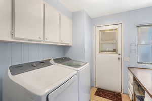 Clothes washing area featuring light tile patterned floors, washer and dryer, and cabinets