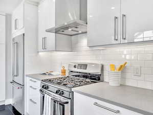 Kitchen featuring tasteful backsplash, ventilation hood, white cabinets, dark tile patterned flooring, and stainless steel appliances