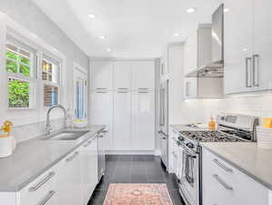 Kitchen with sink, appliances with stainless steel finishes, wall chimney exhaust hood, dark tile patterned floors, and white cabinetry