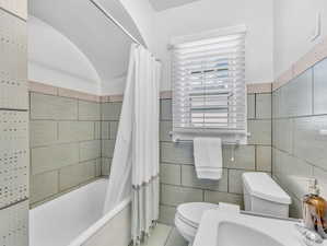 Bathroom featuring tile patterned flooring, tile walls, toilet, and shower / bathtub combination with curtain