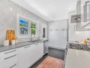 Kitchen featuring sink, dark tile patterned flooring, stainless steel dishwasher, range with gas stovetop, and white cabinets