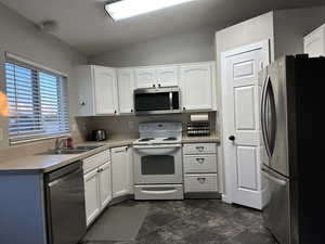 Kitchen with white cabinets, dark tile patterned flooring, sink, and stainless steel appliances