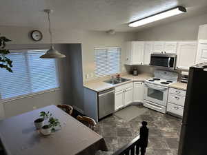 Kitchen featuring sink, hanging light fixtures, dark tile patterned flooring, stainless steel appliances, and lofted ceiling