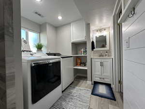 Washroom with light hardwood / wood-style flooring, cabinets, washing machine and dryer, sink, and a textured ceiling