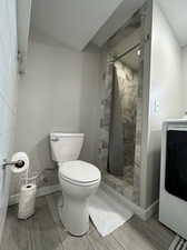 Bathroom with a textured ceiling, toilet, a tile shower, and washer / clothes dryer