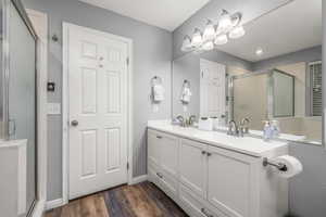 Bathroom featuring a shower with shower door, dual bowl vanity, and wood-type flooring