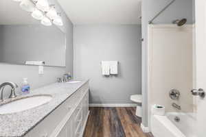 Full bathroom featuring toilet, shower / bathing tub combination, hardwood / wood-style floors, and dual bowl vanity