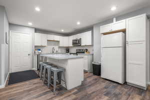 Kitchen with white cabinetry, appliances with stainless steel finishes, dark wood-type flooring, and a kitchen island