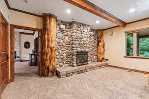 Unfurnished living room featuring carpet flooring, a stone fireplace, and beam ceiling