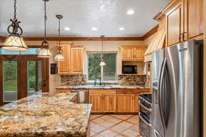 Kitchen featuring decorative backsplash, appliances with stainless steel finishes, light stone counters, light tile patterned floors, and decorative light fixtures