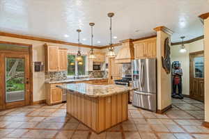 Kitchen featuring backsplash, light stone countertops, light brown cabinetry, a kitchen island, and stainless steel appliances