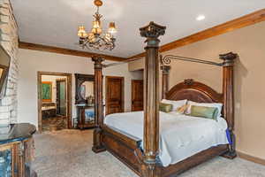 Bedroom featuring carpet flooring, a textured ceiling, ensuite bath, and an inviting chandelier