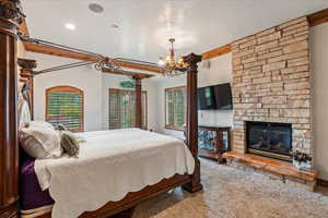 Carpeted bedroom featuring beam ceiling, a notable chandelier, a textured ceiling, and a fireplace