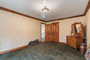 Unfurnished bedroom featuring crown molding, a textured ceiling, and dark carpet